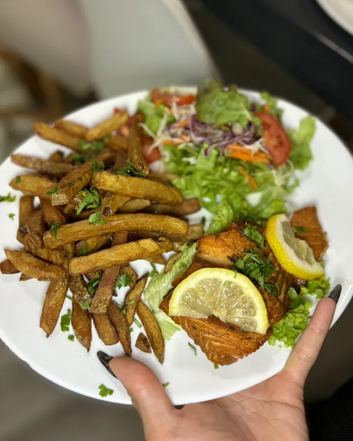 Filet grillé au citron, frites et salade composée, tendu par une main